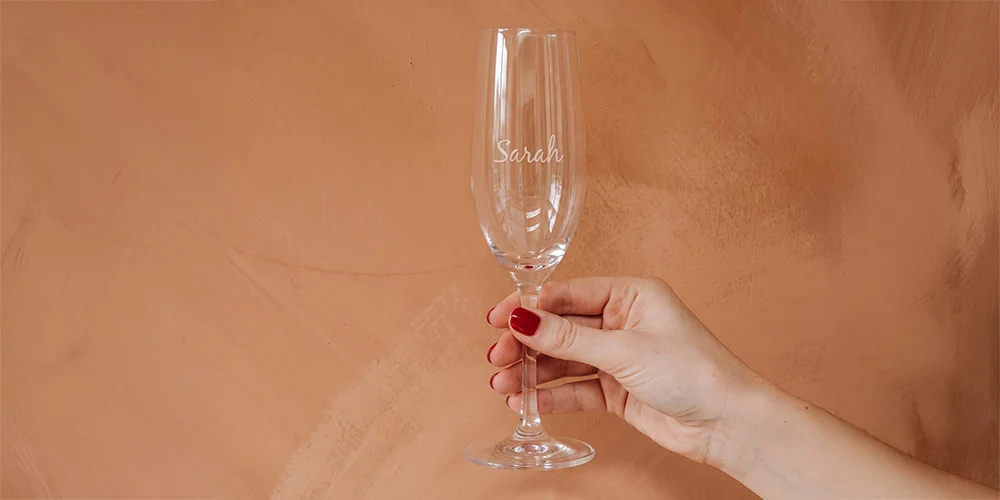 Sektglas mit Namen Sarah Hand mit roten Fingernägeln orangenem Hintergrund